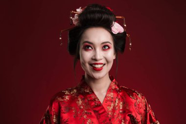 Geleneksel Japon kimonosu giymiş güzel genç bir geyşa resmi. Kırmızı arka planda izole edilmiş gülümsüyor.