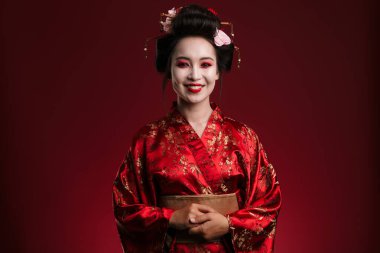 Geleneksel Japon kimonosu giymiş güzel genç bir geyşa resmi. Kırmızı arka planda izole edilmiş gülümsüyor.