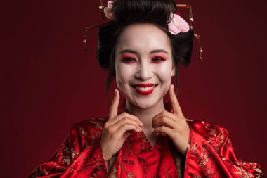 Geleneksel Japon kimonosu giymiş güzel genç bir geyşa resmi. Kırmızı arka planda izole edilmiş gülümsüyor.