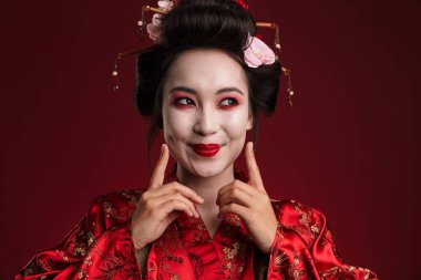 Geleneksel Japon kimonosu giymiş güzel genç bir geyşa resmi. Kırmızı arka planda izole edilmiş gülümsüyor.