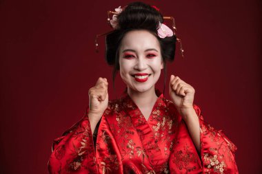 Geleneksel Japon kimonosu giymiş güzel genç bir geyşa resmi. Kırmızı arka planda izole edilmiş gülümsüyor.
