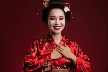 Geleneksel Japon kimonosu giymiş güzel genç bir geyşa resmi. Kırmızı arka planda izole edilmiş gülümsüyor.