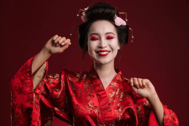 Kırmızı arka planda geleneksel Japon kimonosuyla dans eden güzel genç bir geyşa resmi.
