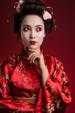 Geleneksel Japon kimonolu çekici Asyalı bir geyşanın kırmızı arka planda izole edilmiş çenesine dokunuşu.