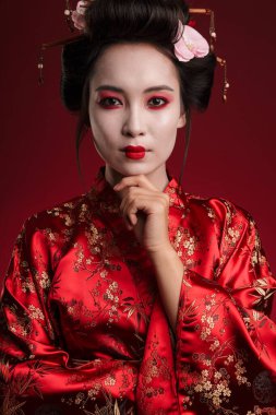 Geleneksel Japon kimonolu çekici Asyalı bir geyşanın kırmızı arka planda izole edilmiş çenesine dokunuşu.