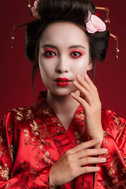 Kırmızı arka planda izole edilmiş geleneksel Japon kimonosuyla dans eden çekici bir geyşa kadın resmi.