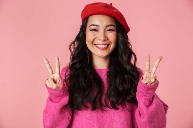 Pembe arka planda barış parmaklarını gösteren uzun siyah saçlı güzel Asyalı bir kız resmi.