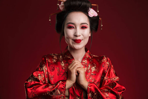 Image of beautiful young geisha woman in traditional japanese kimono isolated over red background