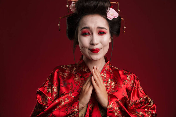 Image of beautiful young geisha woman in traditional japanese kimono smiling isolated over red background