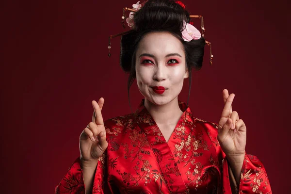 穿着日本传统和服的漂亮的年轻艺妓女人用手指在红色背景下相互交叉的图像 — 图库照片
