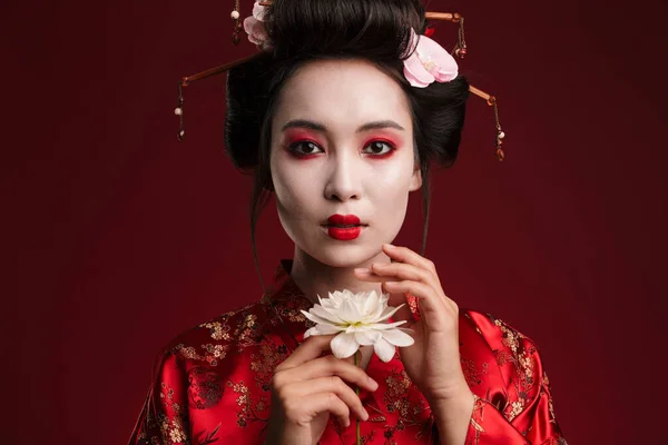 日本传统和服中美丽的艺妓女人在红色背景下抱着花朵的照片 — 图库照片