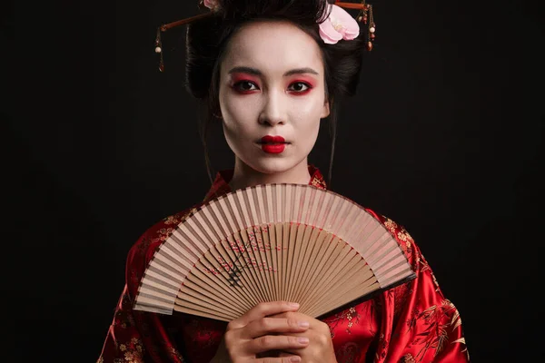照片中身穿日本传统和服的年轻艺妓 手持木制手扇 与黑色背景隔离 — 图库照片