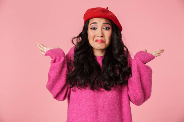 Image of confused beautiful asian girl with long dark hair wearing beret throwing up arms isolated over pink background