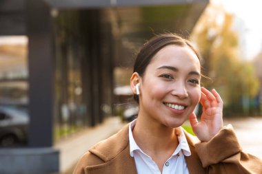 Şehir caddesinde yürürken kulaklık takan Asyalı genç esmer kadın.