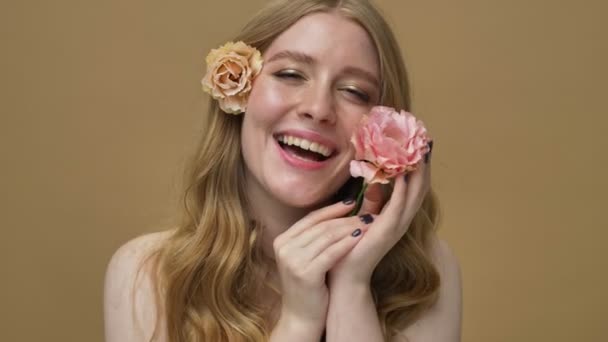一个笑着 半裸着 留着长发的年轻女子 一边摆着美丽的花朵 一边把它们抱在脸上 因为米色的背景而与世隔绝 — 图库视频影像