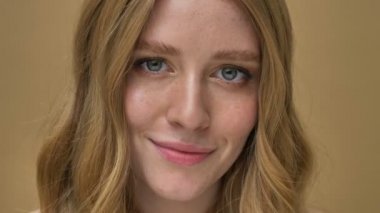 Bej arka planda izole edilmiş kameraya gülümseyen güzel bir genç kadının yakın çekim görüntüsü