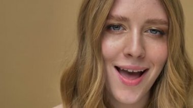 Çekici ve gülen genç bir kadının yakın plan görüntüsü bej arka planda izole edilmiş kameraya göz kırpıyor.