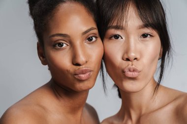 Gri arkaplanda öpüşen iki yarı çıplak kadının portresi.