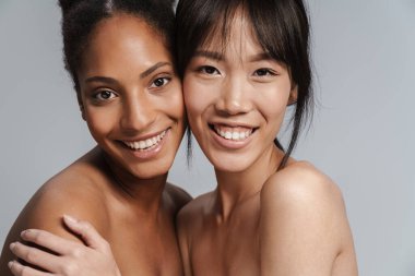 İki çok uluslu yarı çıplak kadının portresi. Gri arka planda sarılıp gülüyorlar.