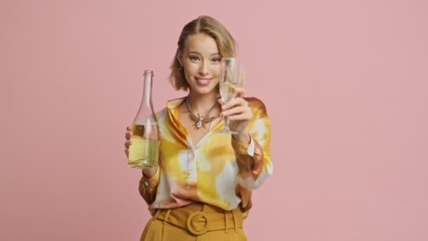 穿着五颜六色的漂亮衣服的快乐漂亮的金发女人 带着粉红的背景 在相机前斟上一杯香槟 — 图库视频影像