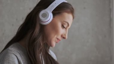 Kulaklıklı, güzel, esmer bir kadın müzik dinliyor ve evde koltukta otururken akıllı telefon kullanıyor.