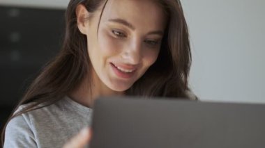 Evdeki masada otururken dizüstü bilgisayar kullanan güzel, esmer bir kadın.