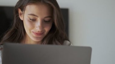 Gözlüklü güzel esmer kadın evdeki kanepenin yanında otururken dizüstü bilgisayar kullanıyor.