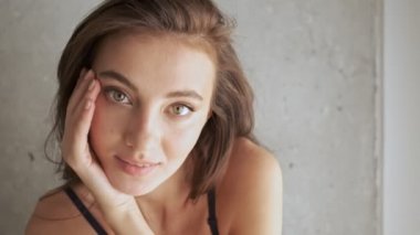 İç çamaşırlı, neşeli, esmer bir kadının, poz verip kameraya bakışının yakın görüntüsü.