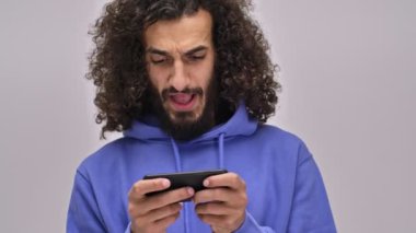 Uzun kıvırcık saçlı neşeli, sakallı, esmer bir adam telefonuyla oynuyor. Stüdyonun gri duvarında yatay olarak izole bir şekilde tutuyor.