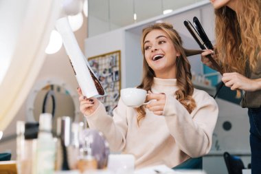 Salonunda saç stilisti olan mutlu, pozitif, güzel bir bayan müşterinin görüntüsü..