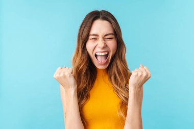 Güzel, neşeli bir kadının portresi. Kazanan olarak bağırıyor ve işaret ediyor. Stüdyodaki mavi arka planda izole edilmiş.