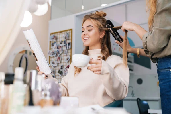 一个年轻漂亮的金发姑娘在美容院里和理发师喝咖啡的照片 — 图库照片
