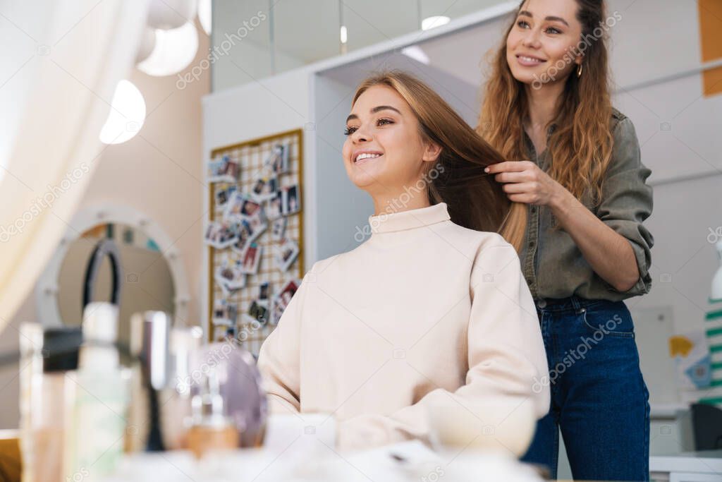 Image of a young happy positive beautiful amazing blonde girl indoors in beauty salon with hairdresser.