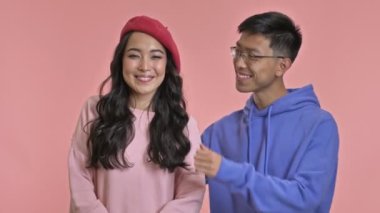 Kız arkadaşının yanaklarıyla oynayan Asyalı genç bir adam pembe duvar arkasında izole edilmiş..