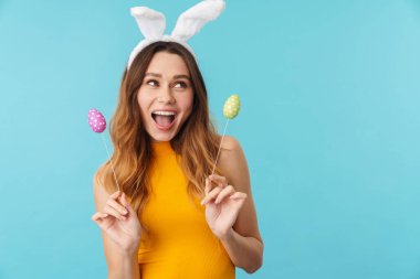 Neşeli, heyecanlı genç bir kızın portresi. Mavi arka planda izole bir şekilde duruyor. Paskalyayı kutluyor.