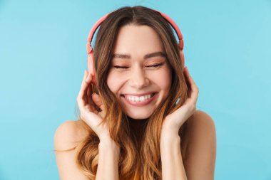 Kulaklık takan güzel, neşeli bir kadının portresi stüdyoda mavi arka planda izole edilmiş müzik dinliyor.