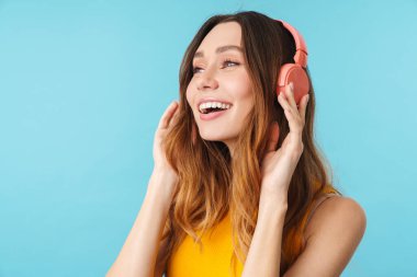 Kulaklık takan güzel, neşeli bir kadının portresi stüdyoda mavi arka planda izole edilmiş müzik dinliyor.