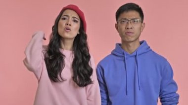 Pembe duvar arkasında izole edilmiş, orta parmağını gösteren genç, negatif, kızgın bir çift..