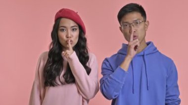 Pembe duvar arkasında izole edilmiş genç bir çift sessizlik jesti gösteriyor..