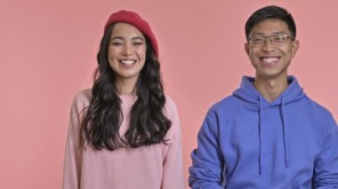 Genç, neşeli, güler yüzlü bir çift pembe duvar arkasında izole edilmiş sessiz bir jest sergiliyor..