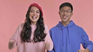 Heyecanlı mutlu çift pembe duvar arkasında izole edilmiş kazanan jest gösteriyor..