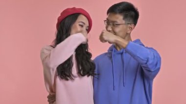 Pembe duvar arkasında izole edilmiş genç bir çift yumruk tokuşturma hareketi yapıyor..