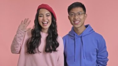 Genç, mutlu, sevgi dolu çift pembe duvarın arkasında sana el sallıyor..