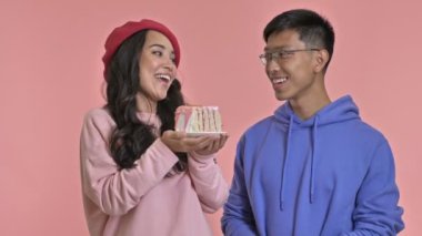 Genç, pozitif bir kadın pembe duvar arkasındaki erkek arkadaşına doğum günü pastası veriyor.