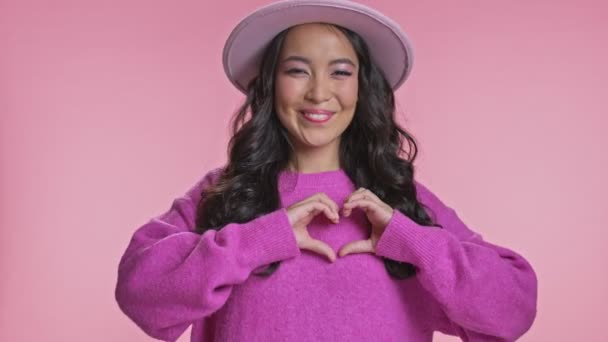 ハッピー可愛いです若いですアジアの女性ポーズ絶縁上ピンク壁の背景ショーハートジェスチャー — ストック動画