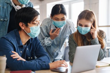 Sınıfta dizüstü bilgisayarla çalışırken koruyucu maske takmış çok uluslu genç öğrencilerin konuşma görüntüleri