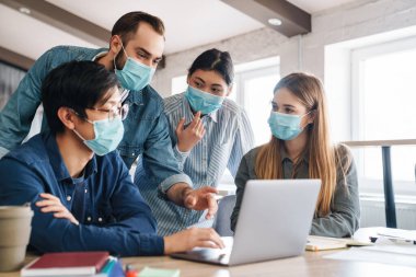 Tıp maskeli çok uluslu genç öğrencilerin sınıfta dizüstü bilgisayarla ders çalışmalarının fotoğrafı.