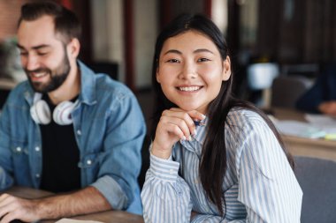Sınıfta çalışırken gülümseyen çok uluslu neşeli öğrencilerin fotoğrafı.