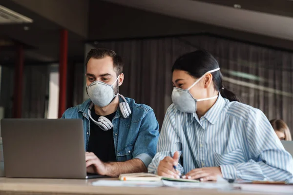 Foto Estudantes Satisfeitos Multinacionais Máscaras Médicas Estudando Com Laptop Sala — Fotografia de Stock