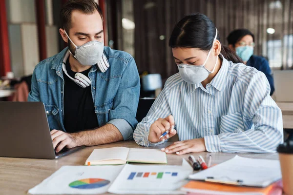 Foto Jovens Estudantes Multinacionais Máscaras Médicas Estudando Com Laptop Sala — Fotografia de Stock